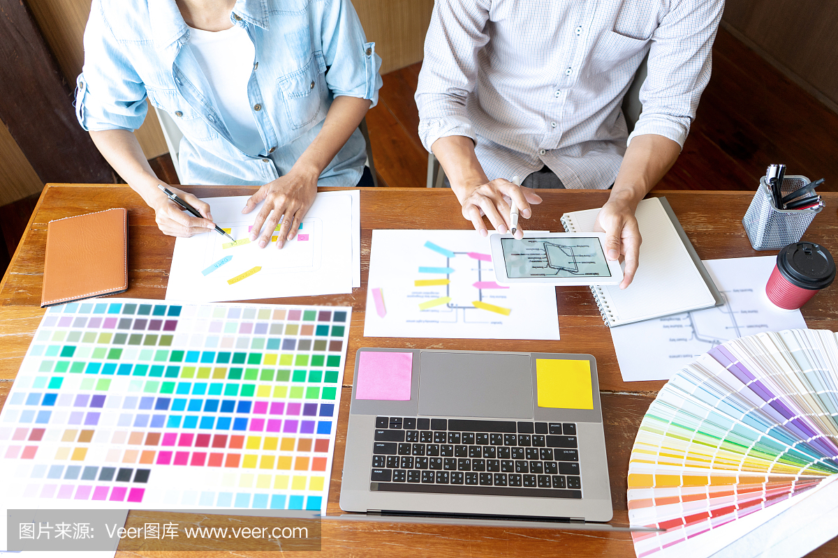 一群年輕的設計師在辦公室工作,設計了一款新產(chǎn)品,使用顏色表和電腦筆記本電腦為新的智能手機設計概念